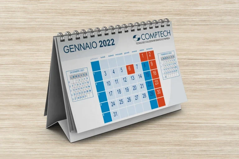 Un calendario da tavolo aperto fino a gennaio 2022, con date evidenziate in blu e rosso, marchiato con il logo Comptech, posto su una superficie di legno.