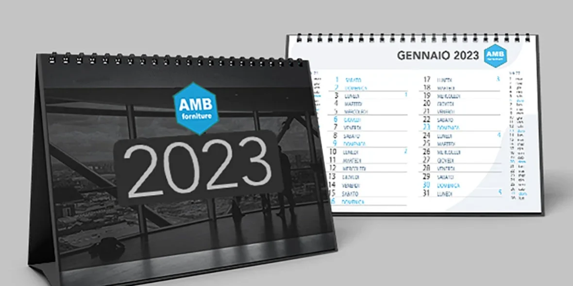 Sono esposti due calendari da tavolo per il 2023, uno che mostra l'anno con il logo di AMB Forniture, l'altro aperto a gennaio con date e nomi elencati in italiano.