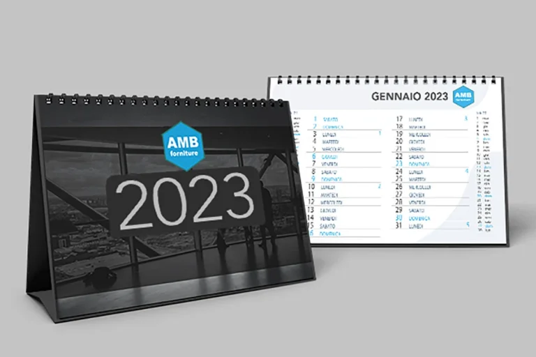 Sono esposti due calendari da tavolo per il 2023, uno che mostra l'anno con il logo di AMB Forniture, l'altro aperto a gennaio con date e nomi elencati in italiano.