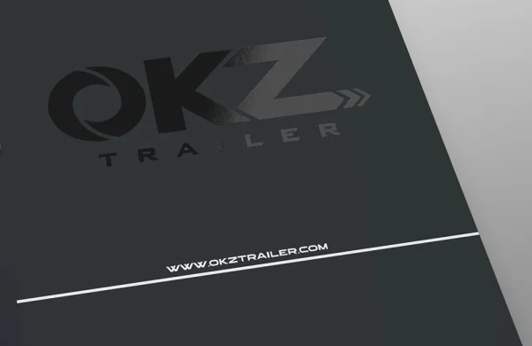 cataloghi nobilitazione UV Primo piano della copertina di un opuscolo scuro con il logo OKZ Trailer e il sito web www.okztrailer.com in testo bianco in basso.
