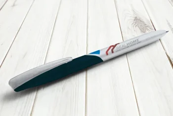 Una penna in bianco e nero con marchio REAL HOME ed eleganti accenti di tipografia poggia su una superficie di legno bianco.