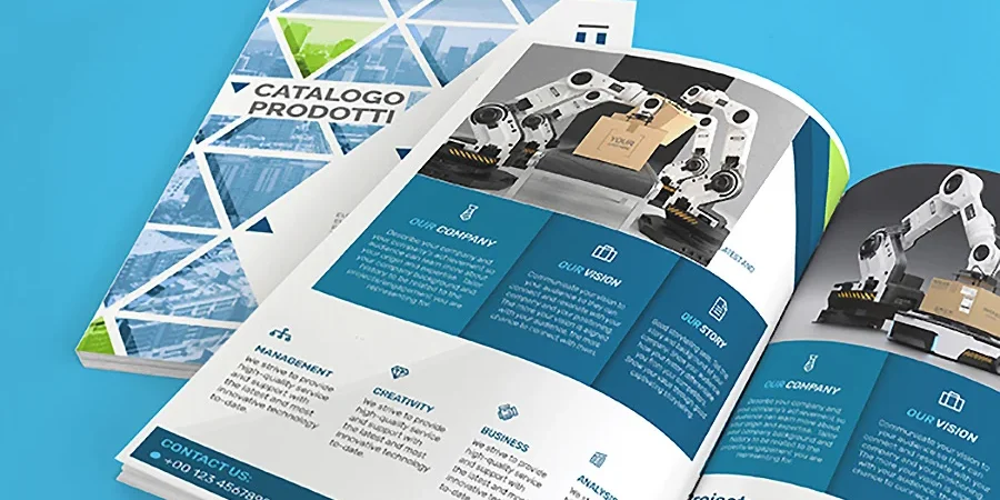 Catalogo di prodotti aperto con immagini di bracci robotici, grafica e sezioni di testo, posto su una superficie blu con accanto un'altra copia chiusa.