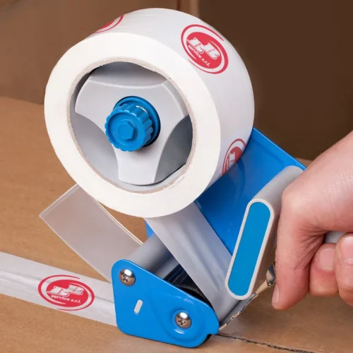 Una mano utilizza un dispenser di nastro adesivo per sigillare una scatola di cartone con nastro da imballaggio bianco contrassegnato da un logo rosso.