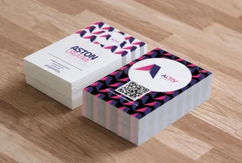 Due pile di biglietti da visita colorati su una superficie di legno, una con il logo ASTON CREATIVE, l'altra con un disegno geometrico, un codice QR e il logo ALTIV.
