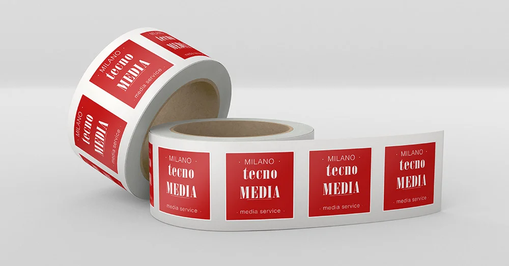 Rotolo di etichette rettangolari bianche e rosse con il testo MILANO tecno MEDIA - media service - su sfondo piatto.