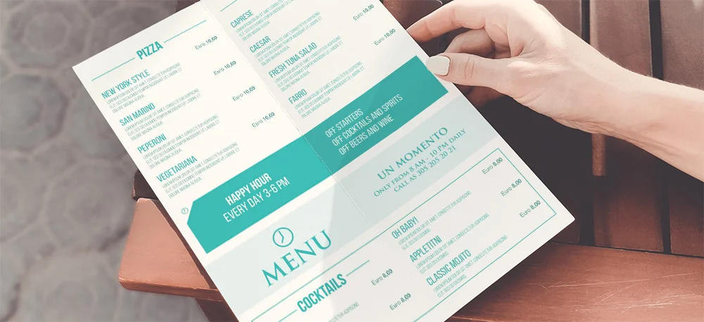 Persona con in mano un menu con sezioni per pizza, cocktail e dessert, con dettagli sull'happy hour e varie opzioni di cibo e bevande elencate in testo verde e nero.