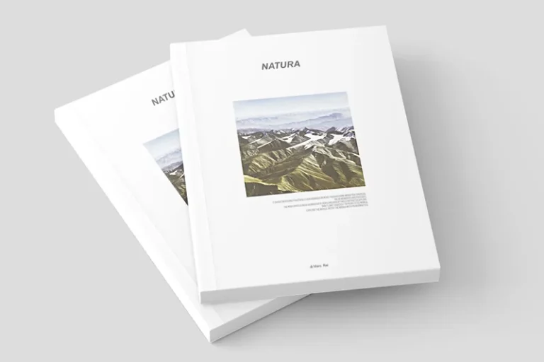 Due riviste bianche impilate intitolate NATURA con una foto di paesaggio montano in copertina, con un elegante design di stampa libri, su uno sfondo grigio chiaro.