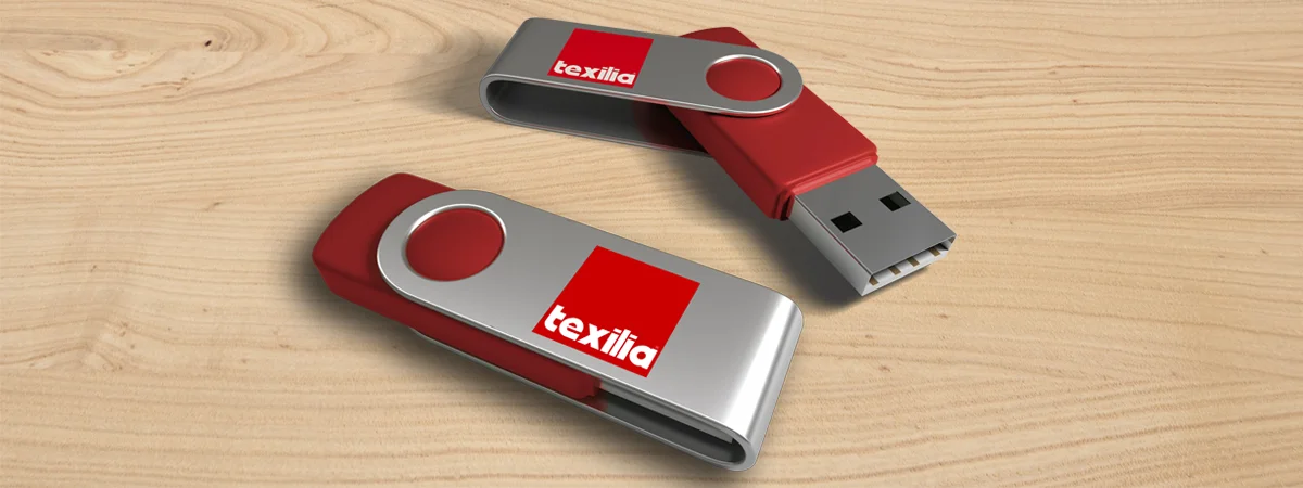 Due chiavette USB rosse e argento con il logo Texilia poggiano su una superficie di legno chiaro.