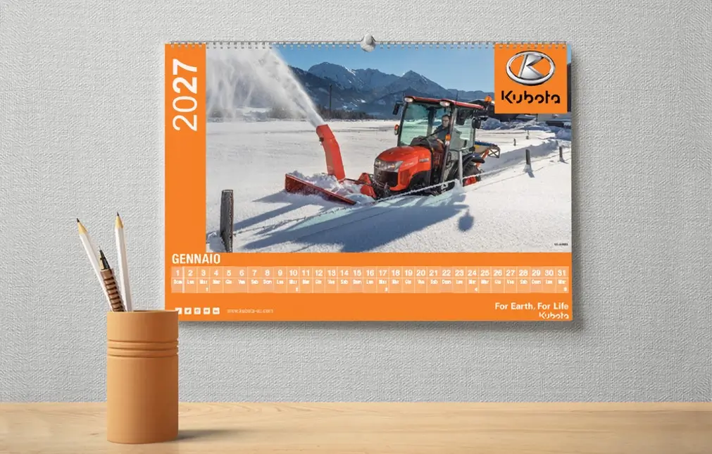 Calendario da parete 2027 con un trattore che sgombra la neve con un accessorio spazzaneve; logo e marchio Kubota visibili; mese italiano Gennaio visualizzato.