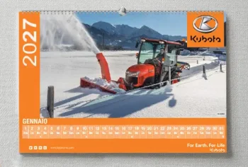 Un trattore Kubota rimuove la neve da una strada rurale con un accessorio spazzaneve; sullo sfondo sono visibili montagne e campi. Bold Tipografia mette in evidenza l'immagine su un calendario da parete 2027 per il mese di gennaio.