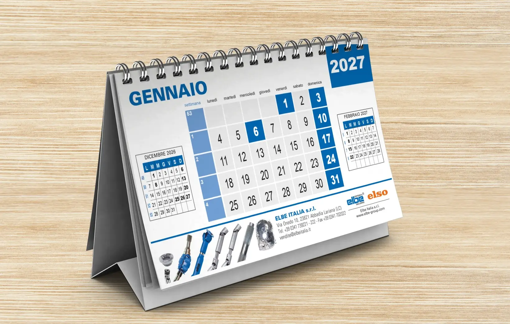 Un calendario a spirale da tavolo mostra il mese di gennaio 2027 in italiano, con i giorni della settimana evidenziati. Il calendario è appoggiato su una superficie di legno.